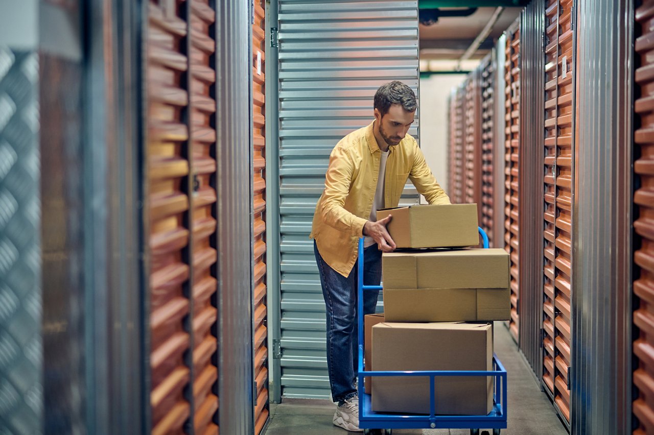 Tranquil concentrated male worker putting the boxed goods on the platform cart