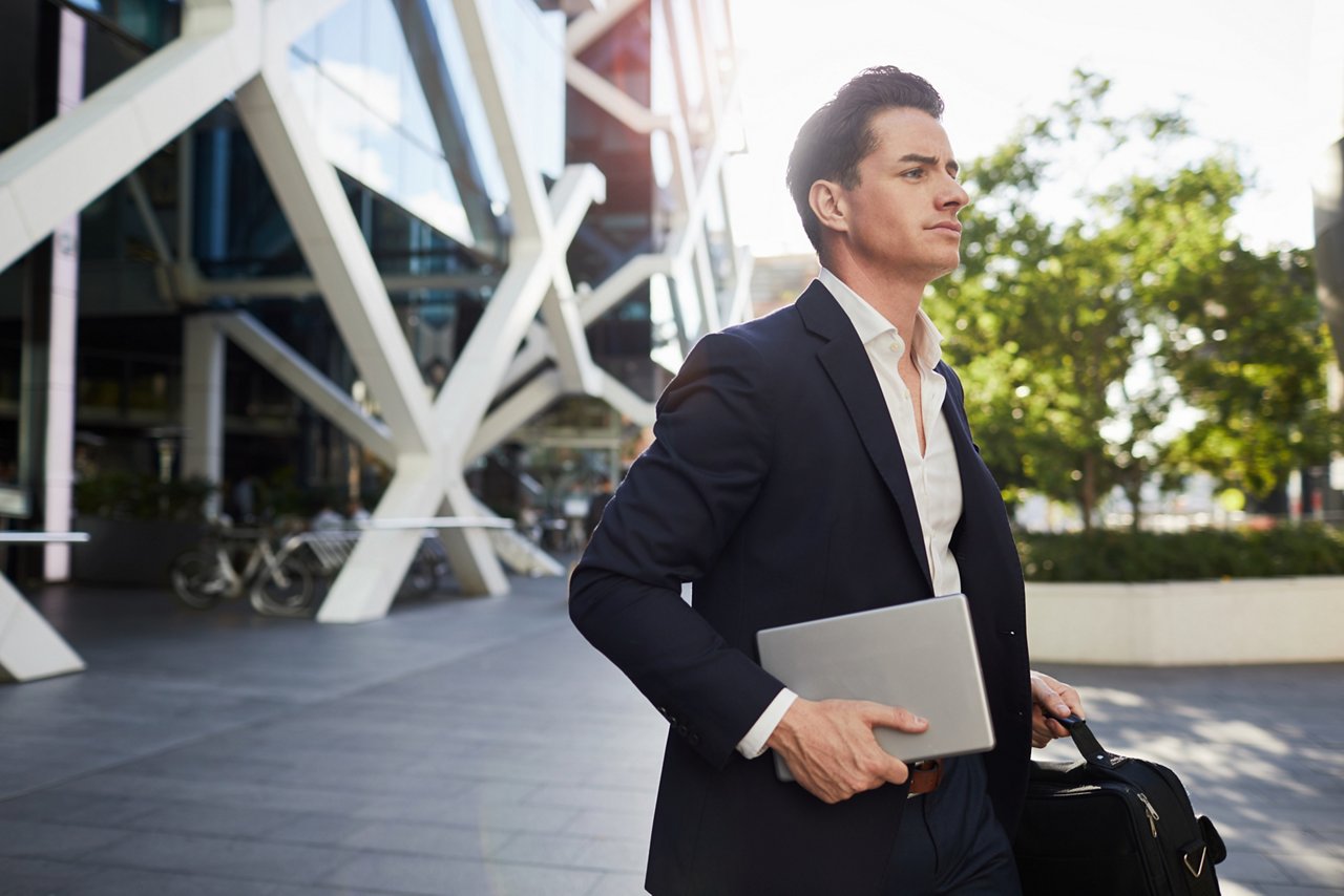 Business man commuting on rush hour. Holding a computer and walking in Sydney.