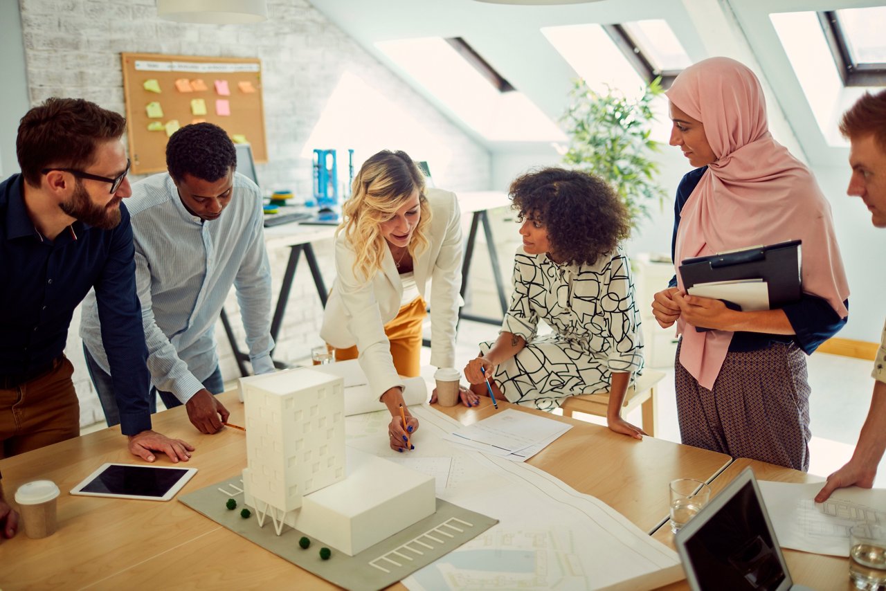 Diverse business team of architects have meeting in the office.Standing i front of blueprints and architectural model and discussing about their new project.
