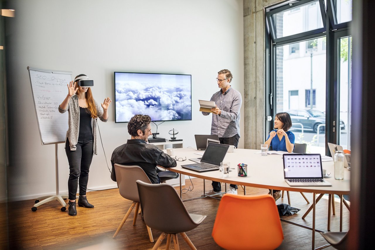 Businesswoman wearing virtual reality headset while giving presentation to team in board room at creative office