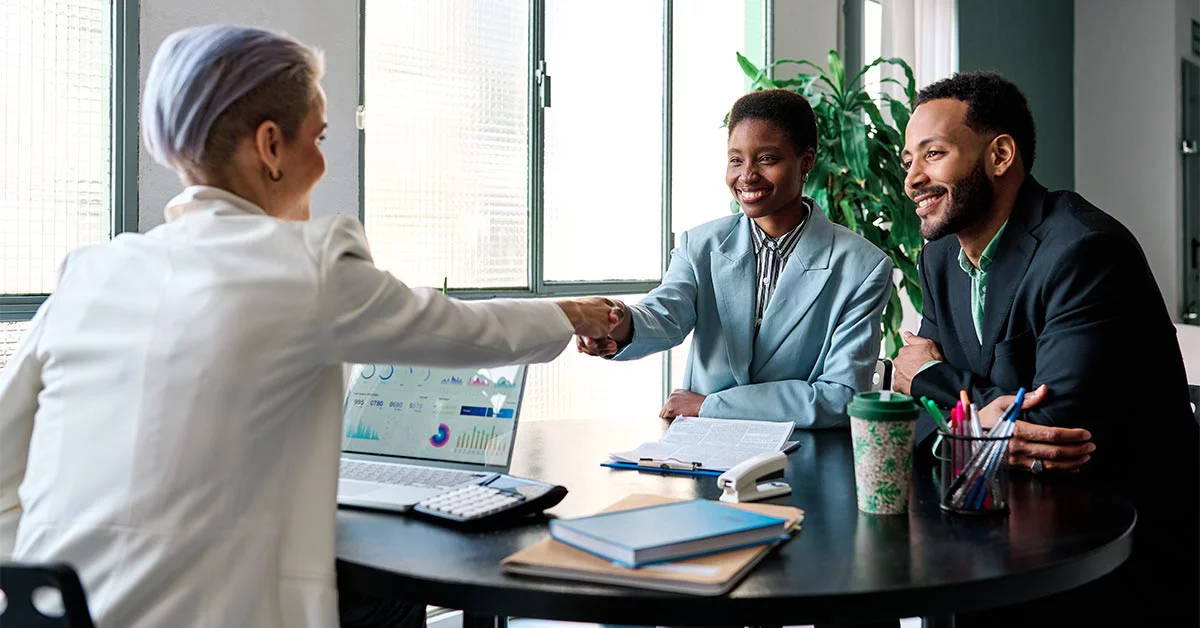 Man and woman meeting with a financial planner . The women is shaking hands with the financial planner.