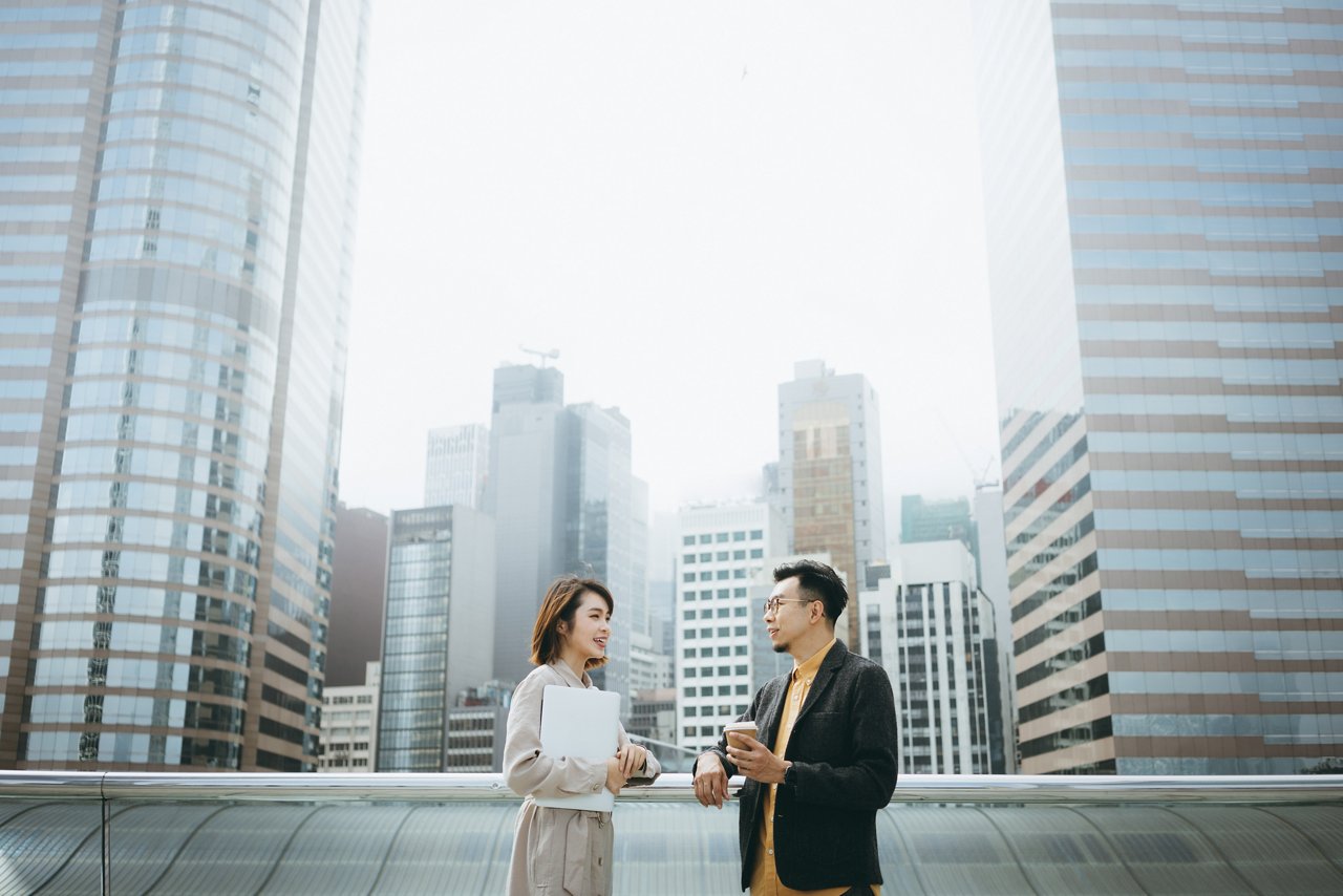 近代的なオフィスビルの前の街の風景を背景に、都会のバルコニーでビジネスプロジェクトに協力しながらノートパソコンを持つ若いプロのビジネスパートナー