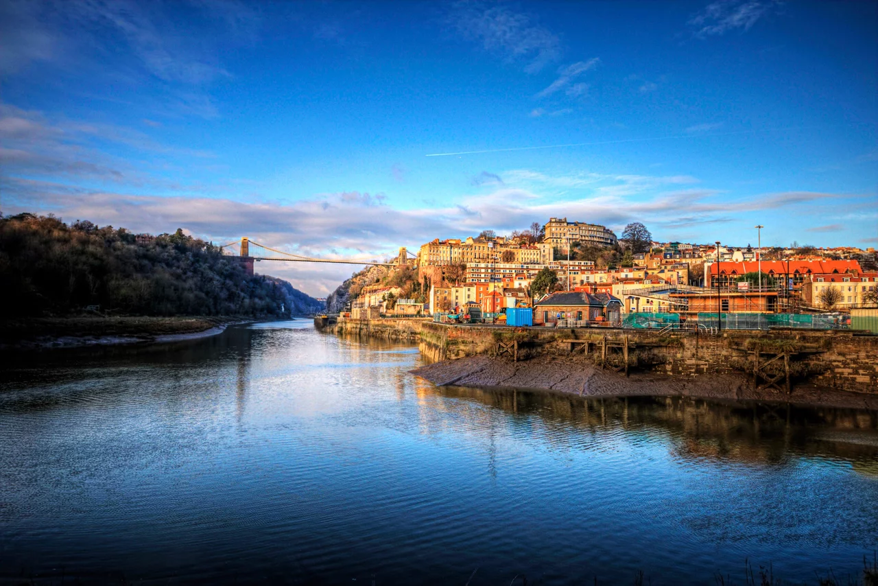 Scenic view of Bristol cityscape with Clifton Suspension Bridge spanning the Avon Gorge under a bright blue sky.