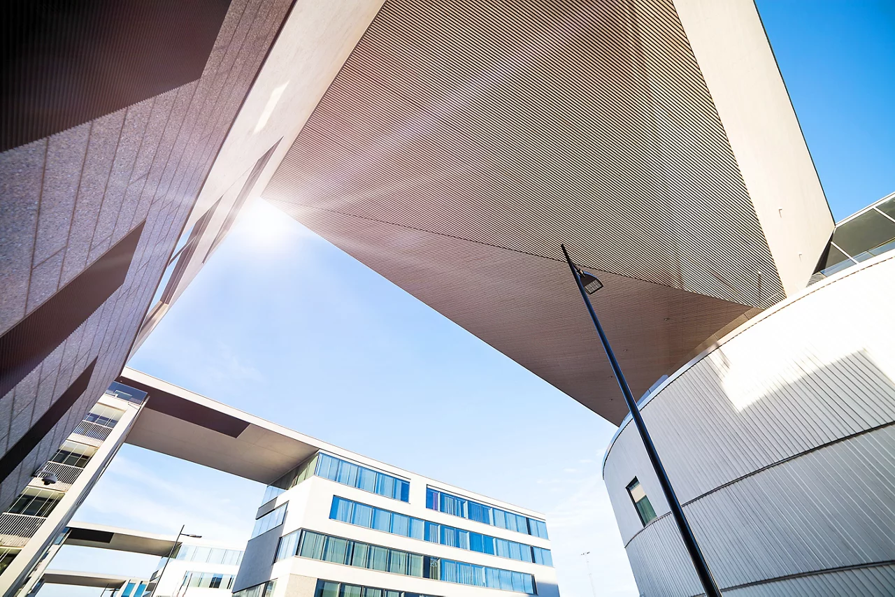  Modern architectural building with angular overhang, blue sky, and geometric shapes. Streetlight visible beneath structure.