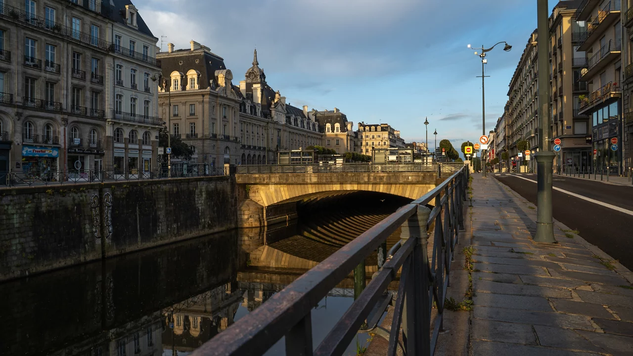 Paysage urbain parisien avec une architecture classique le long du canal, un pont de pierre et la lumière du soir illuminant les bâtiments.