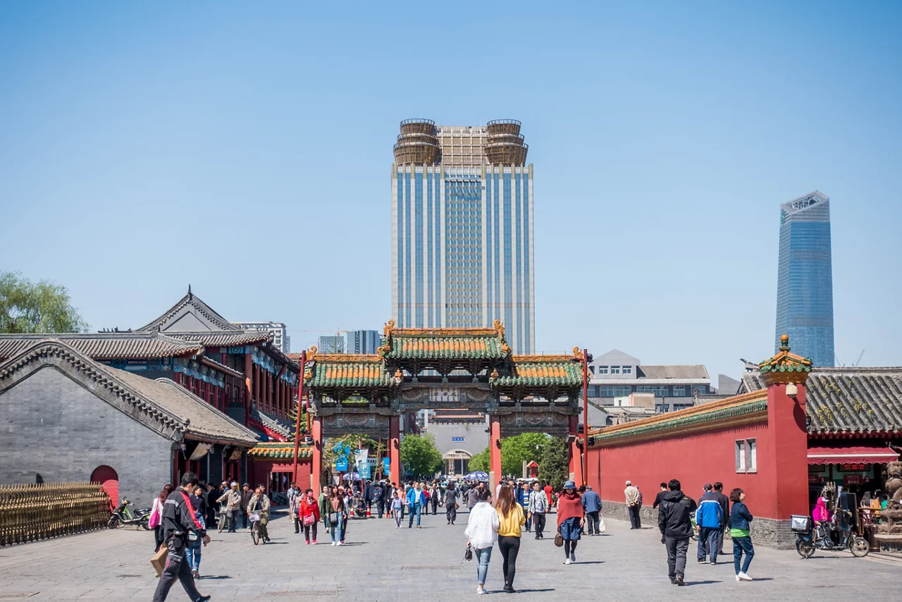 传统的中国寺庙建筑群，有红色的墙壁和华丽的大门，游客熙熙攘攘，还有现代化的摩天大楼。