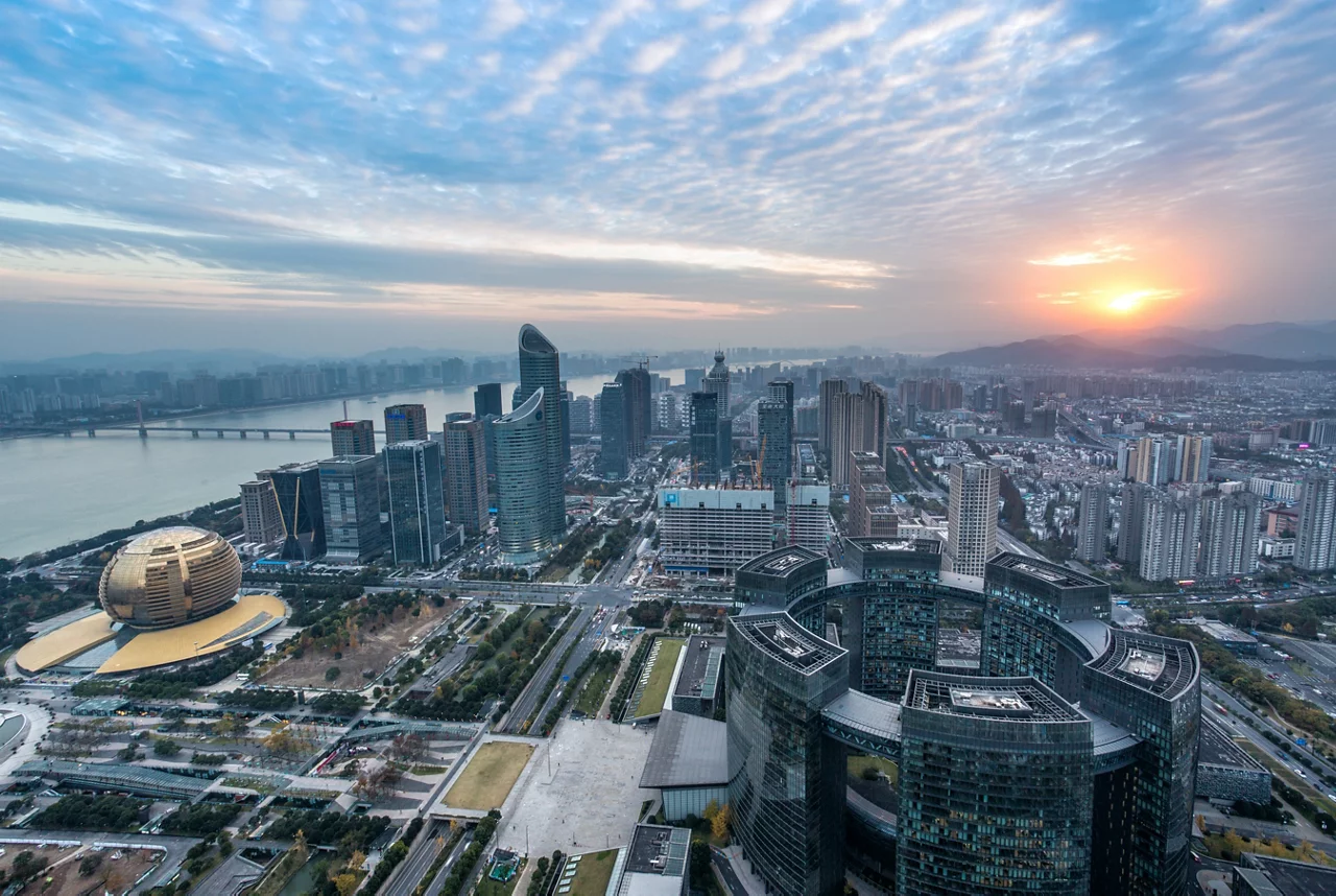 杭州城市天际线鸟瞰图，展示钱江新城现代摩天大楼，夕阳西下，河流穿城而过，云层绚丽。