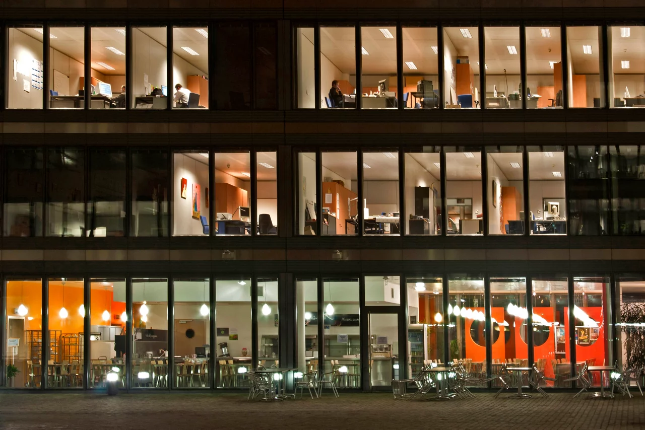 Facade of office building with lit office spaces and empty office canteen.