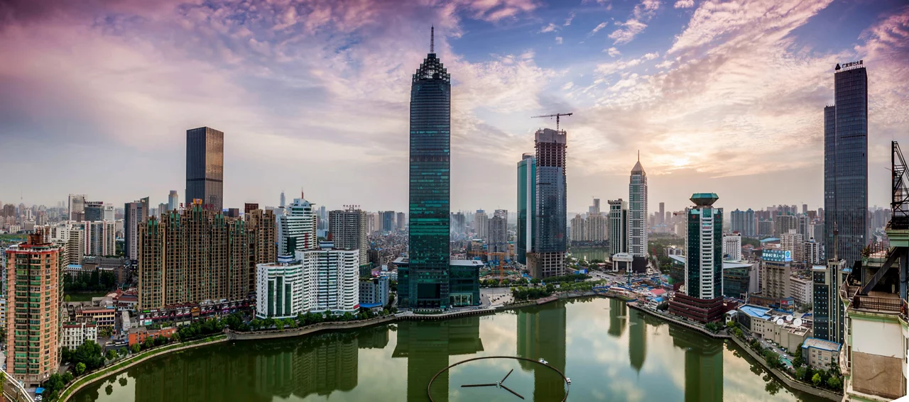 日落时分，五彩缤纷的云彩笼罩着一座现代亚洲城市的全景，高耸的摩天大楼环绕着中央水域。