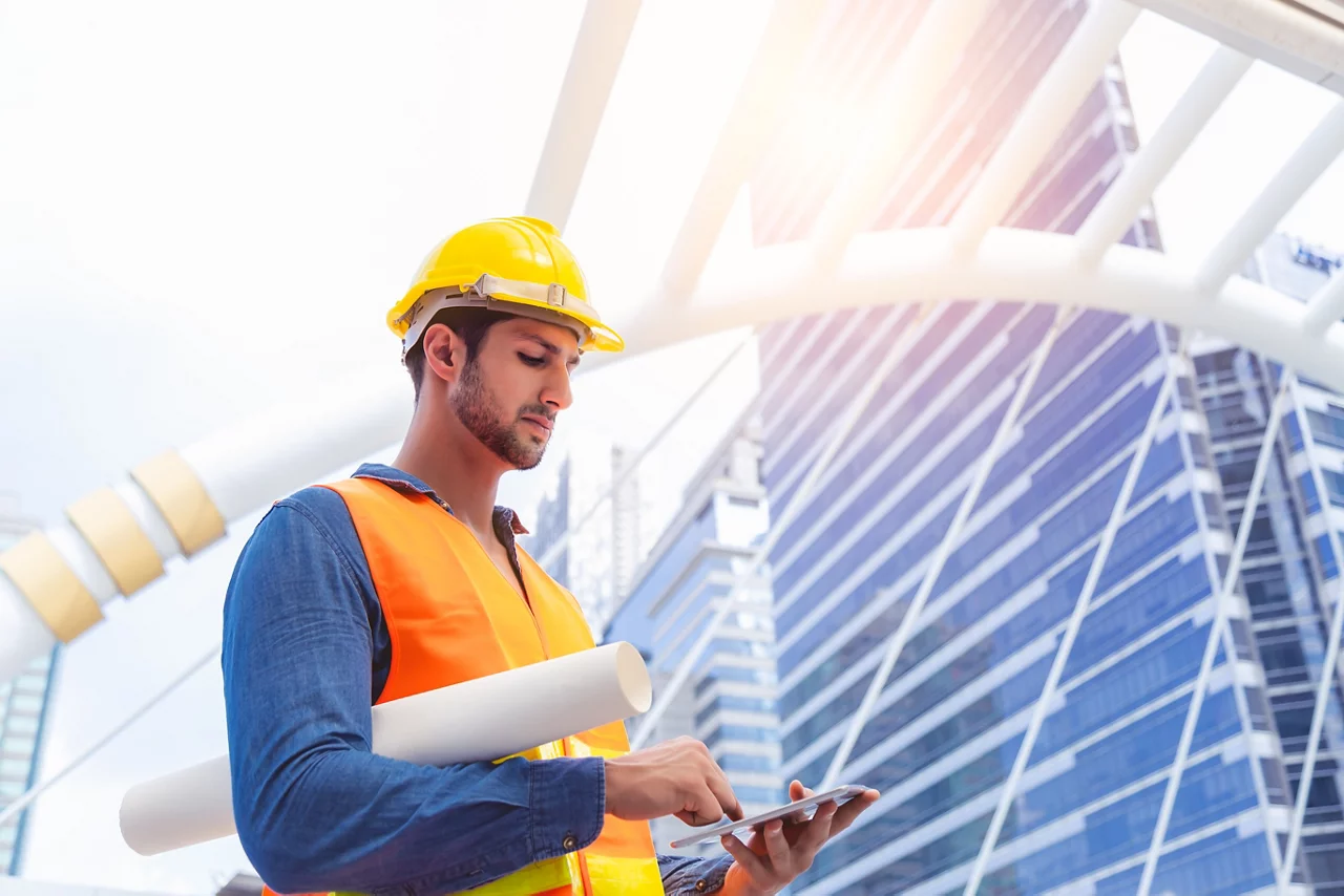 Blue collar worker, engineer man work on digital tablet, hold blue print, wear safety hat, stand near worksite