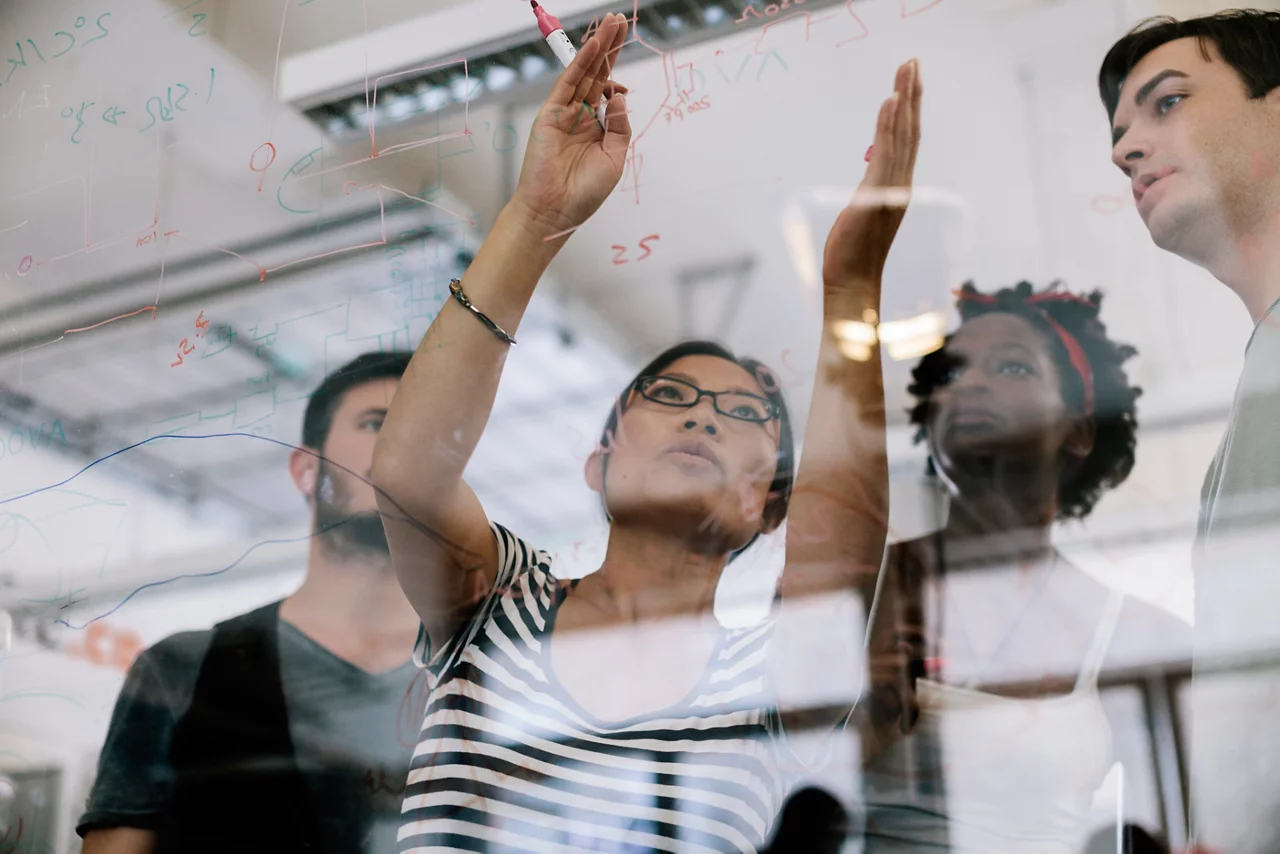 Asian woman leading the discussing of an electronic project. she pointing to electronic schematic on a glass wall