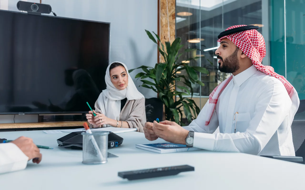 محترفو الأعمال يرتدون الزي التقليدي للشرق الأوسط ويتعاونون في غرفة مؤتمرات حديثة مجهزة بالتكنولوجيا.