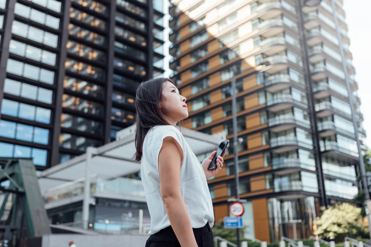 Young Asian businesswoman with smart phone standing in the city centre