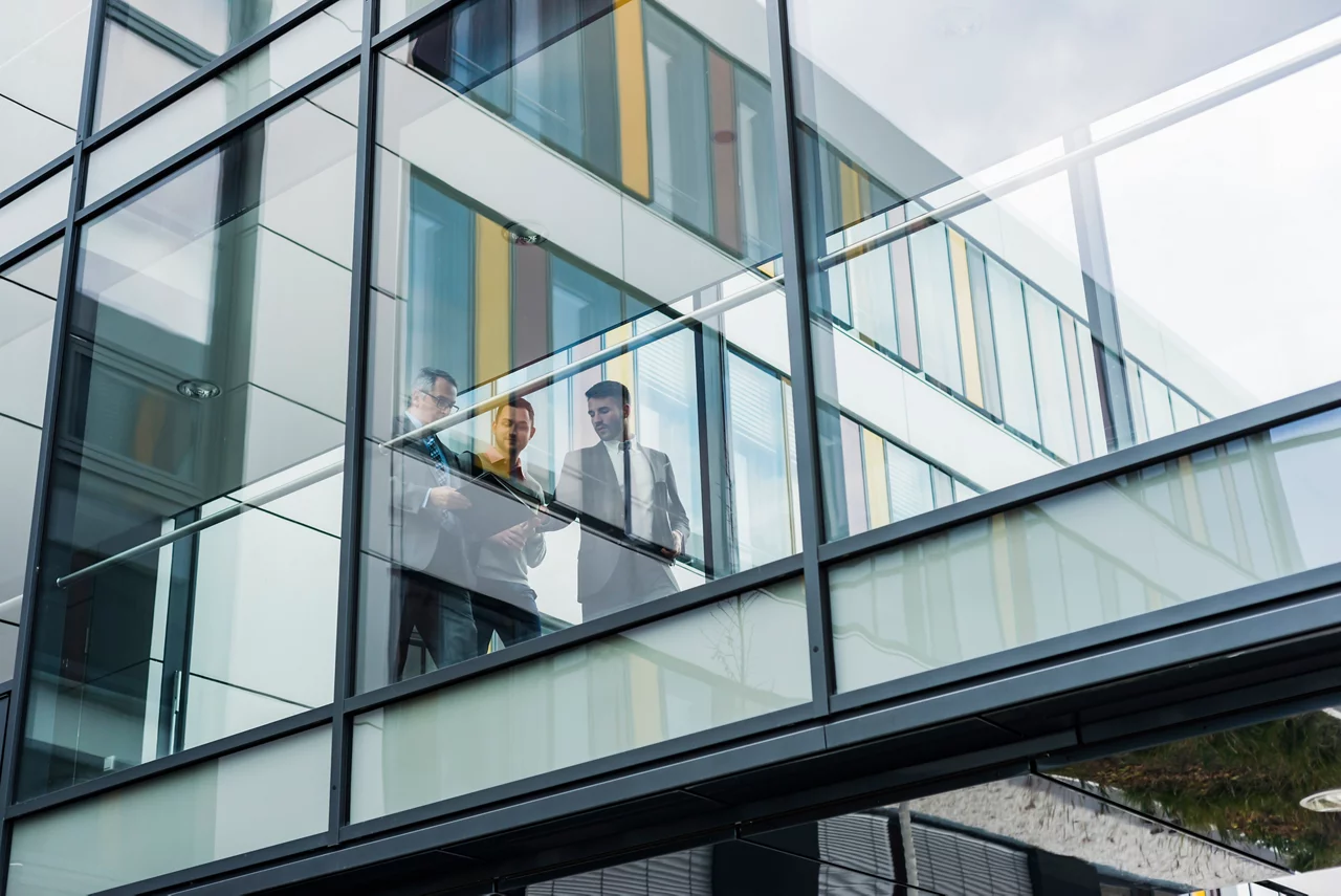Three businessmen behind glass facade, passage