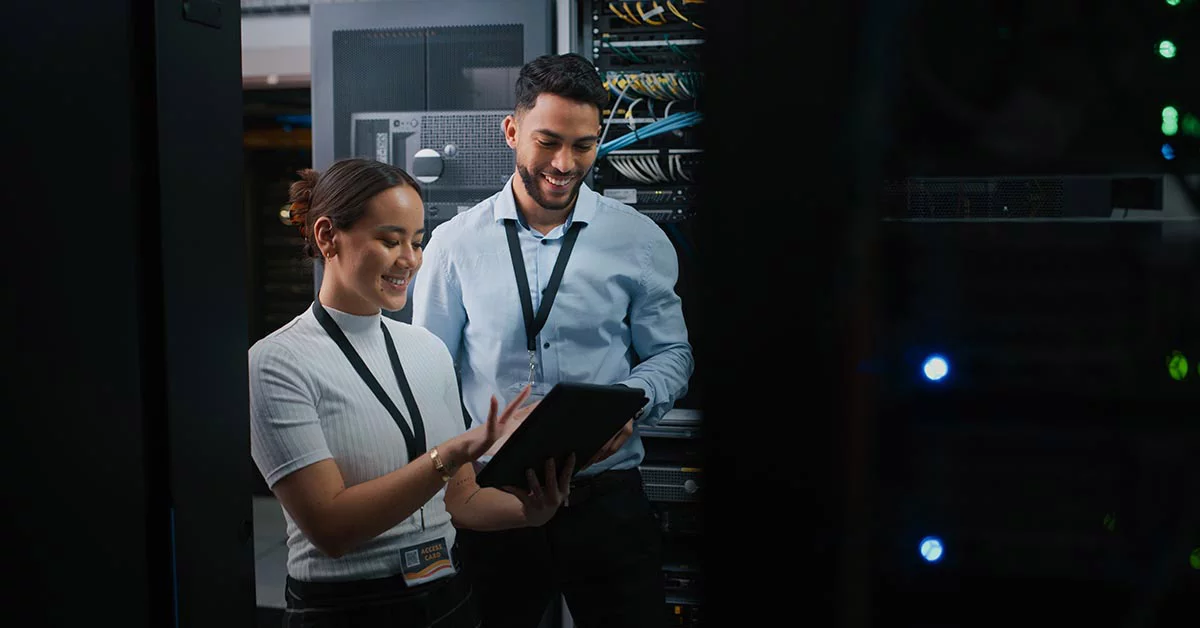 Two employees smiling while looking at the tablet inside data centre