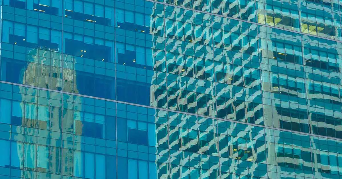 The windows of a building reflect the image of an adjacent structure, highlighting the interplay of light and design.