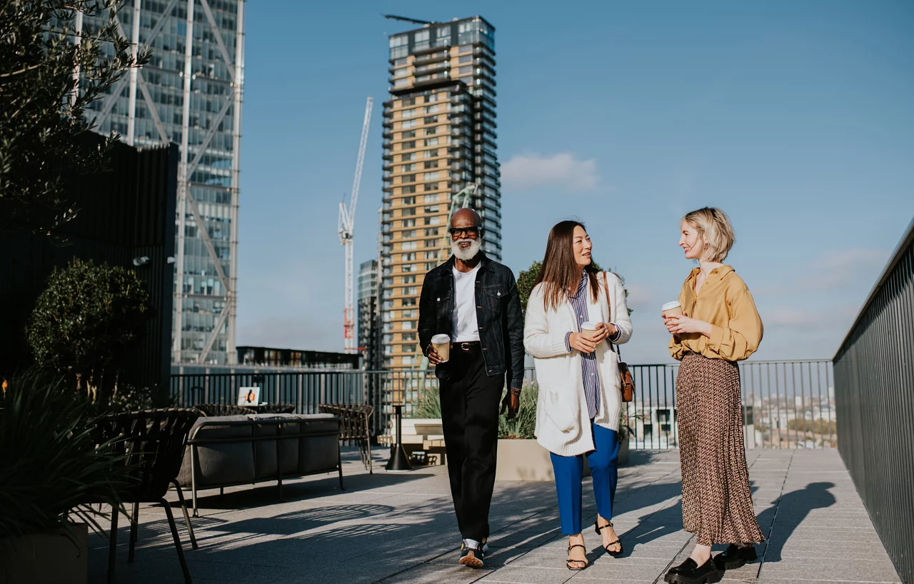 A man and two woman dressed in smart-casual outfits walk beside each other on a roof top terrace