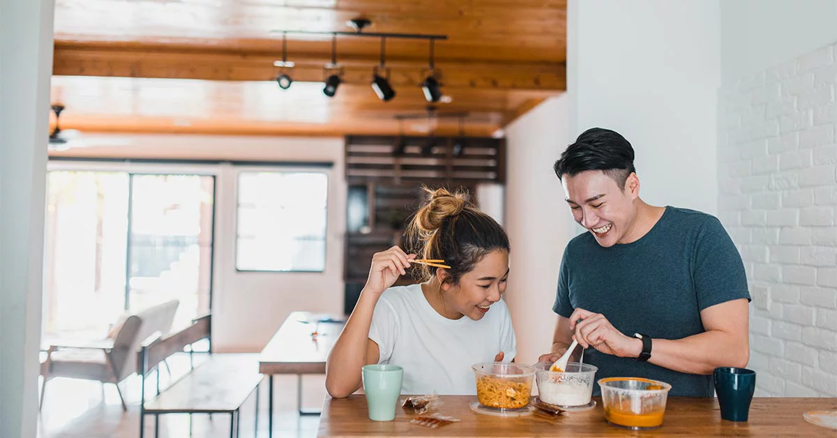 Asian couple laughing and sharing a meal in domestic kitchen