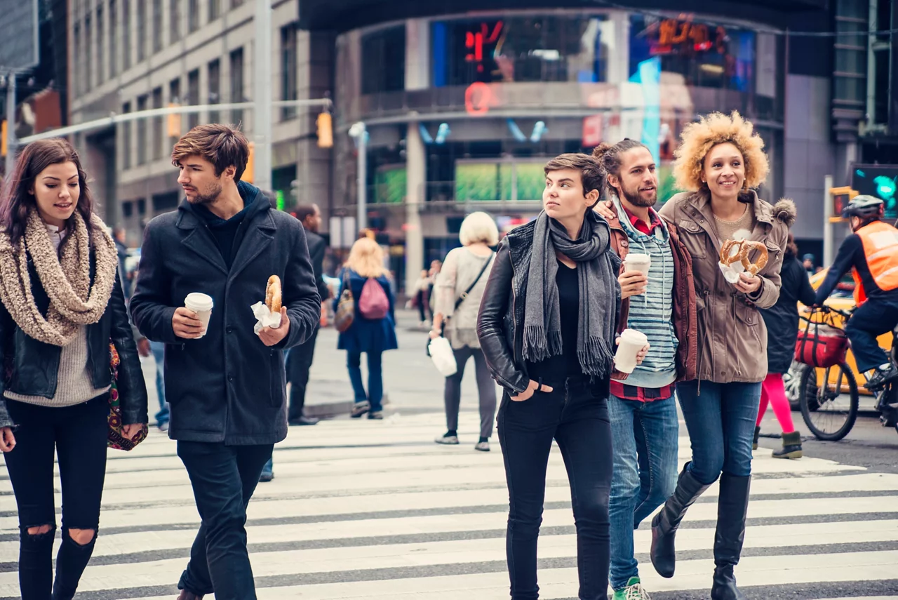 A group of five people, wearing winter clothes, walk across a city street.