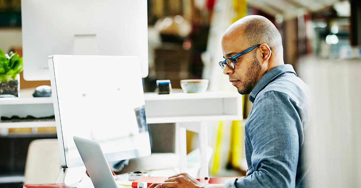 Man wearing glasses working at desk with computer in modern office setting.