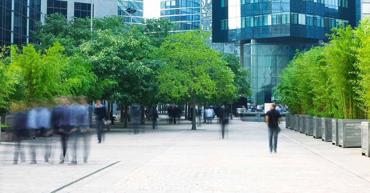 Espace urbain avec immeubles de bureaux modernes, arbres verts et piétons flous marchant sur une place pavée