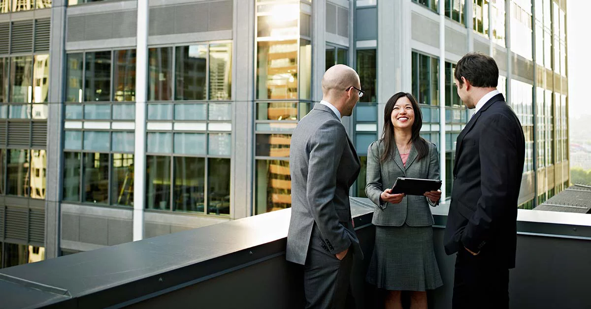 A female professional and two male professionals are engaging in trivial conversation on the balcony of the building