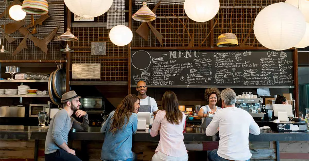 People at a cafe sitting at the bar counter and staff serving coffees - food service concepts