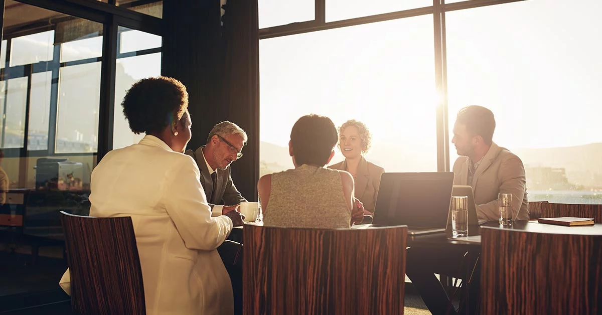 Diverse group of businesspeople sitting together around a table in a boardroom during a late afternoon office meeting