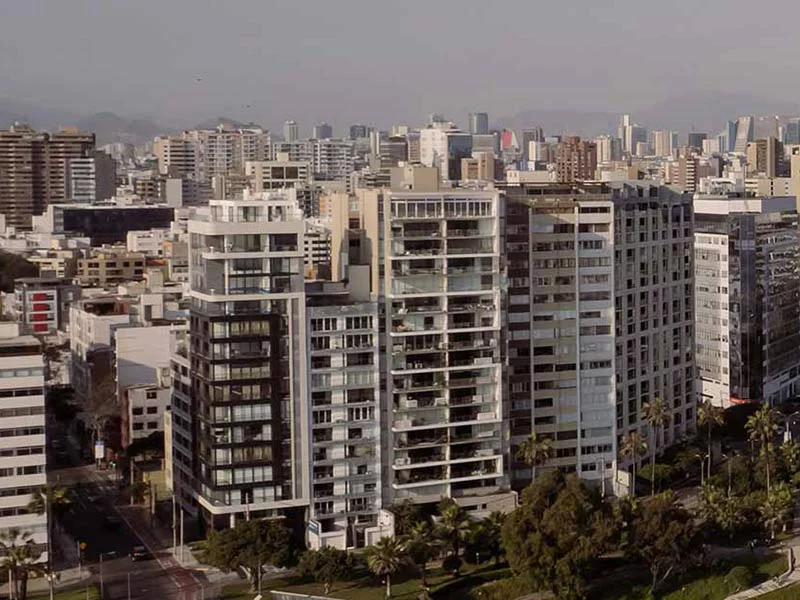 A vibrant city skyline featuring tall buildings surrounded by lush green trees.