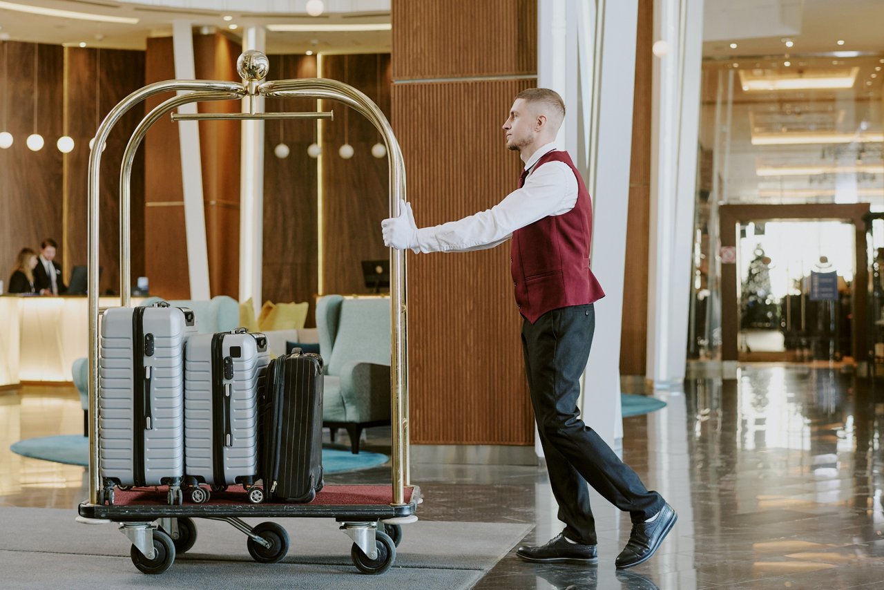 Wide shot of young adult Caucasian man pushing golden luggage cart