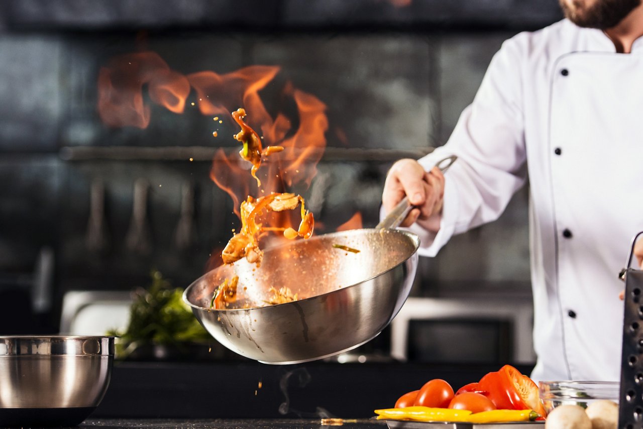 Chef hands keep wok with fire. Closeup chef hands cook food with fire. Chef man burn food at professional kitchen.