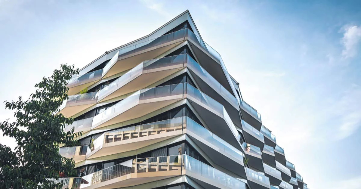 Modern building with angular, wavy balconies and glass railings against a clear blue sky.