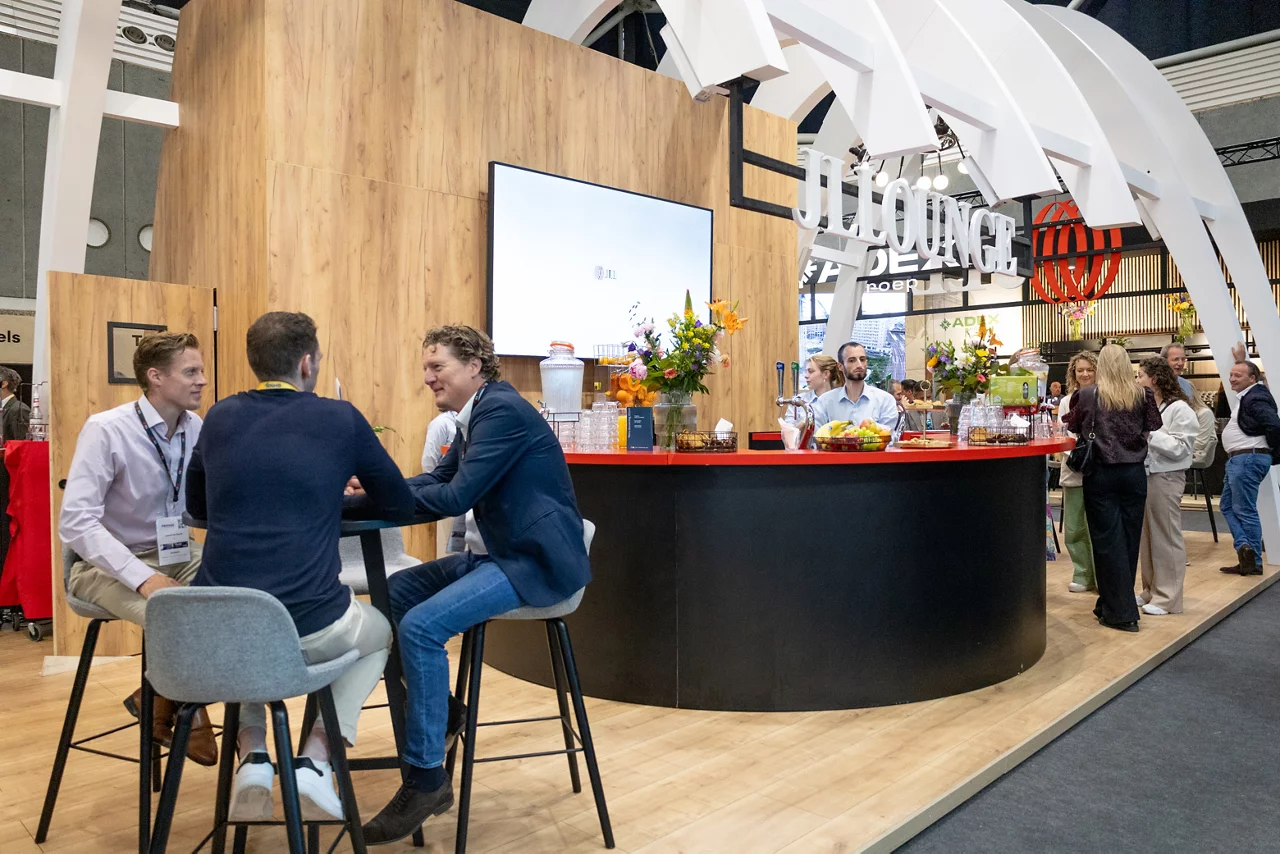 Moderne beurstand met professionals die netwerken rond een gebogen balie en hoge zithoek.