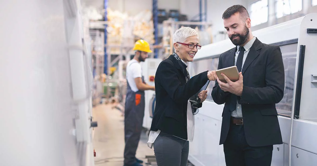 Diverse professionals review information on a tablet while facility professional in a hard hat works on machinery