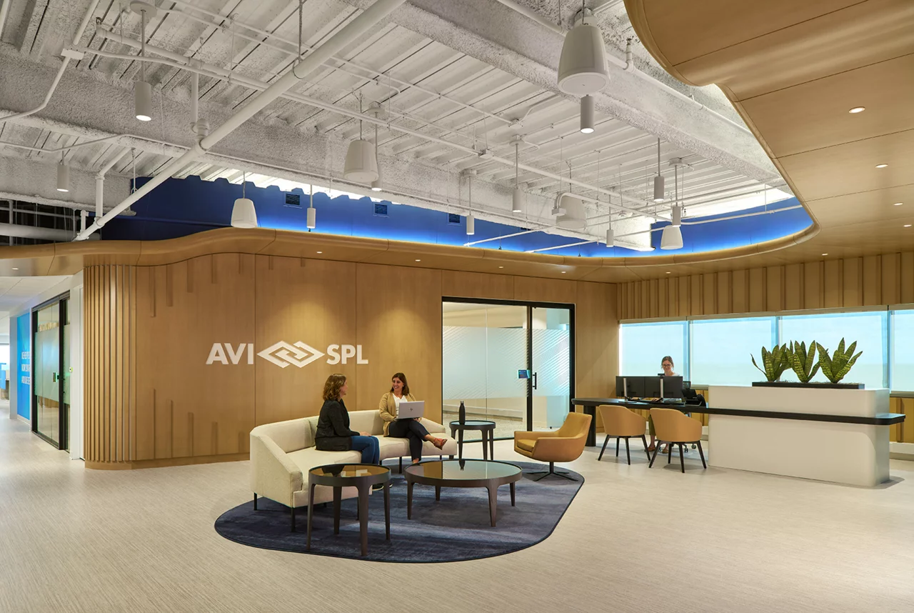 The modern AVI-SPL reception area, with employees meeting in the lobby featuring a branded wood wall and contemporary furniture.