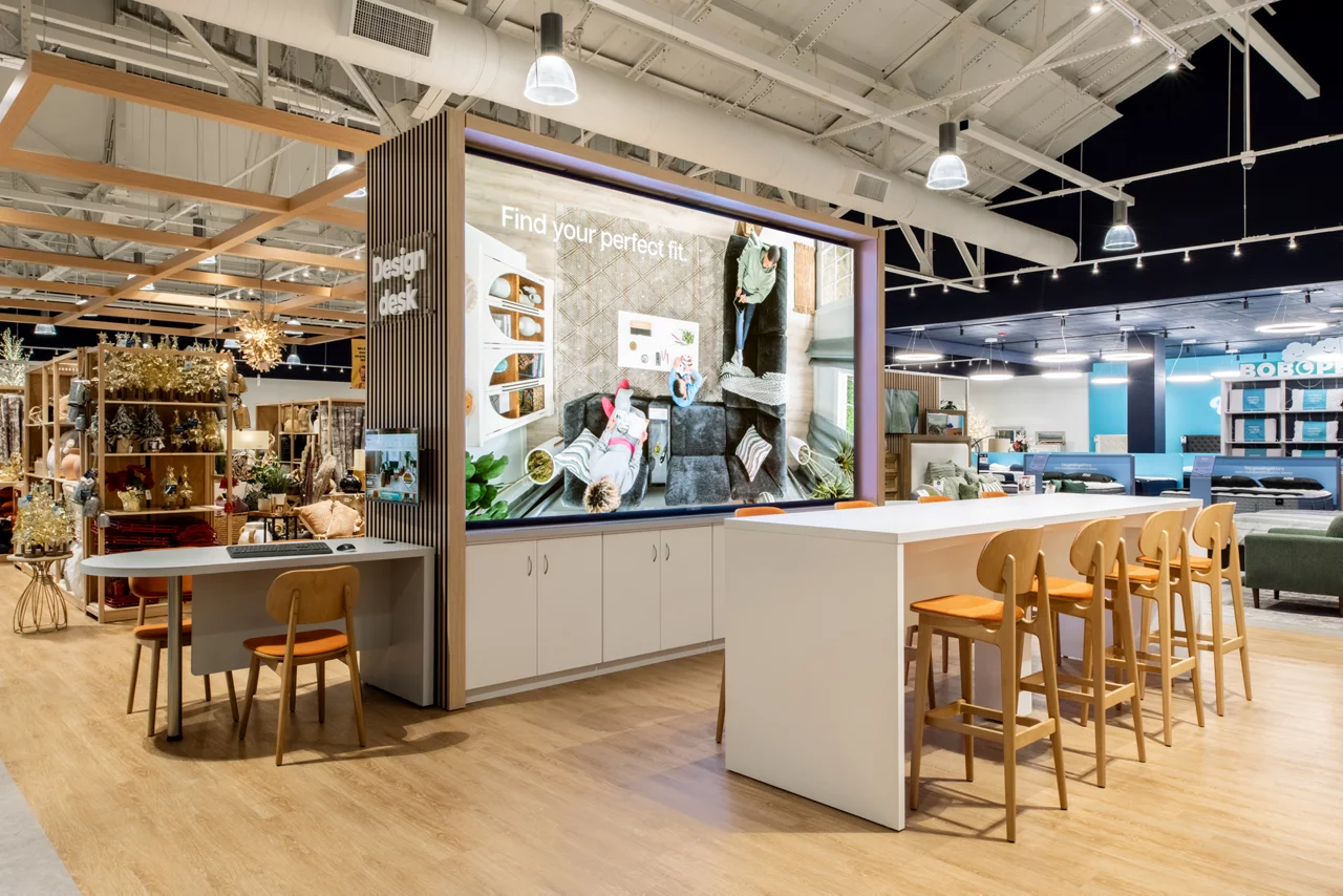 The interactive 'Design Desk' in a Bob's Discount Furniture store, with a large digital screen and customer seating.
