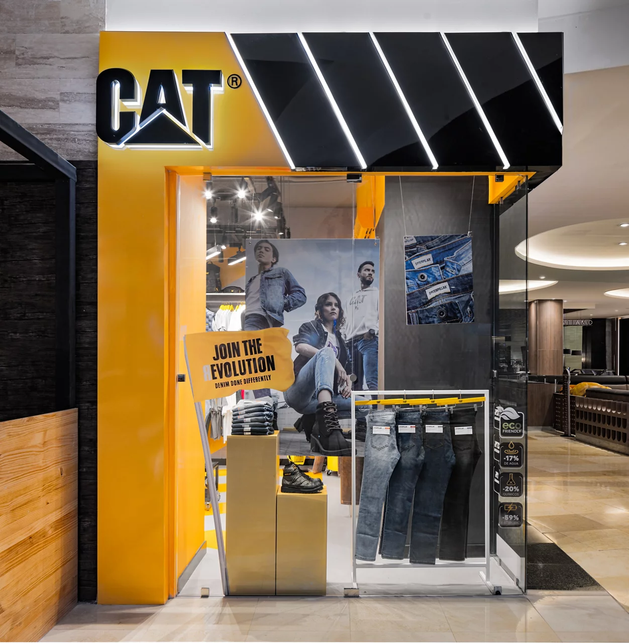 The entrance to a CAT store, featuring a yellow and black design with a window display for its 'Join the Evolution' denim line.
