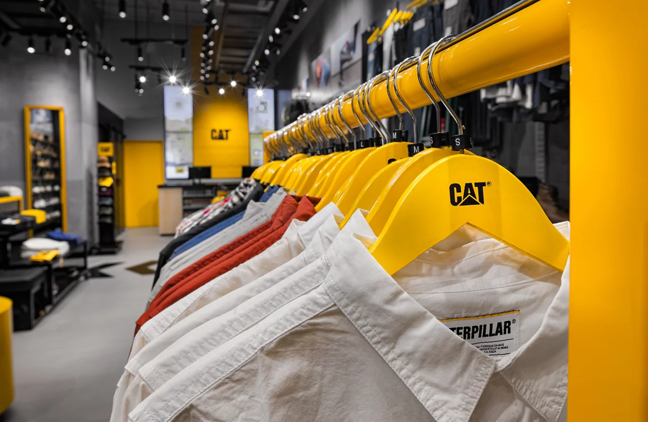 A close-up of a clothing rack with CAT shirts on signature yellow hangers inside the modern retail store.
