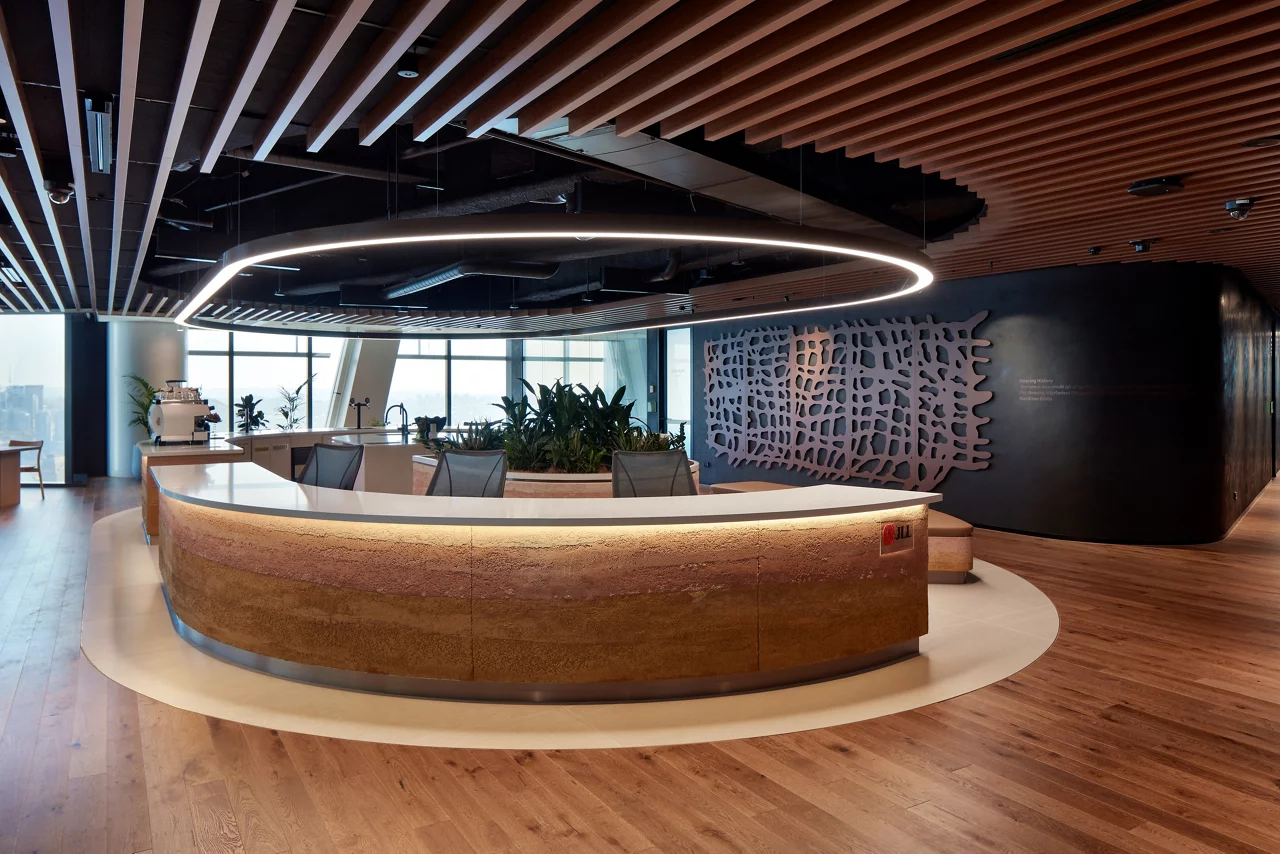 The client hub in JLL's Sydney office, featuring a modern rammed earth concierge desk, wood accents, and large windows.