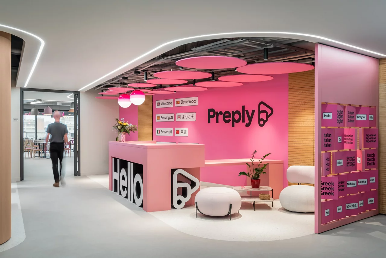 The bright, modern reception area of Preply's office, featuring vibrant pink walls, a 'Hello' desk, and multilingual signs.
