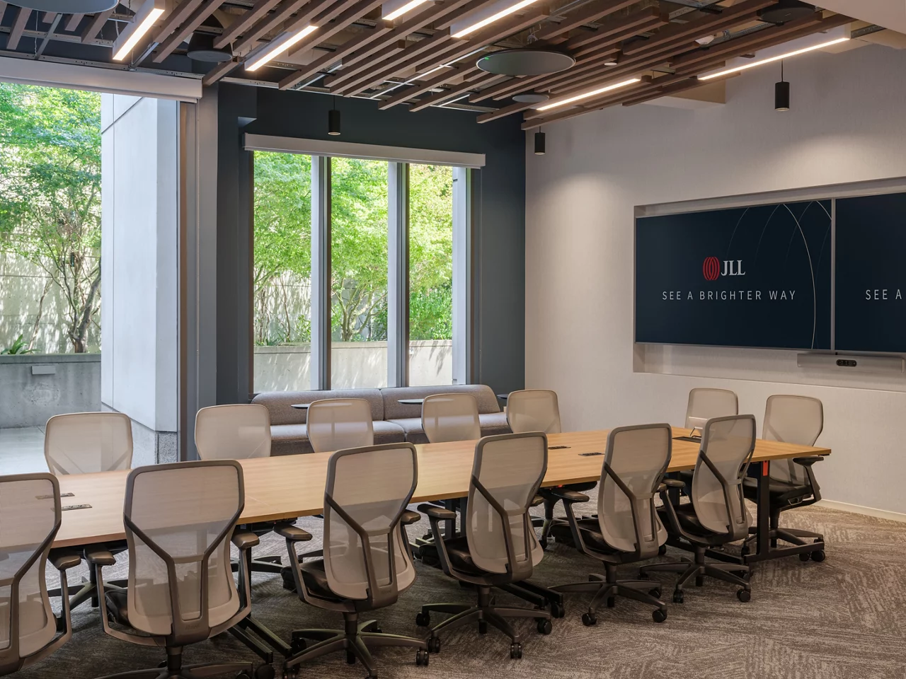 A modern conference room at the JLL Walnut Creek office, featuring a branded screen, modern seating, and patio views.