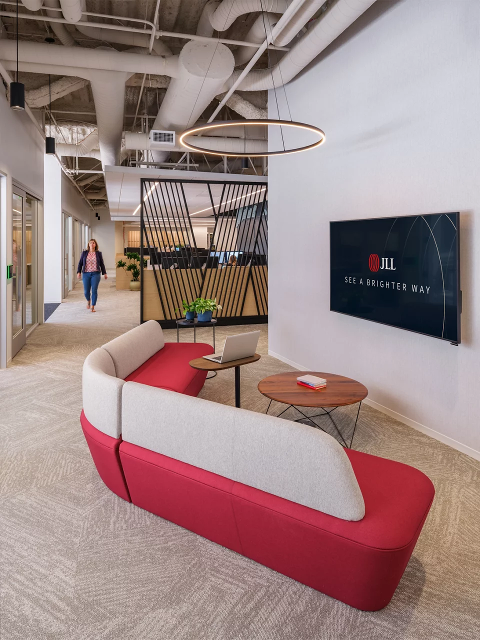 A modern breakout area in the JLL Walnut Creek office with a curved red sofa and a wall-mounted JLL branded screen.