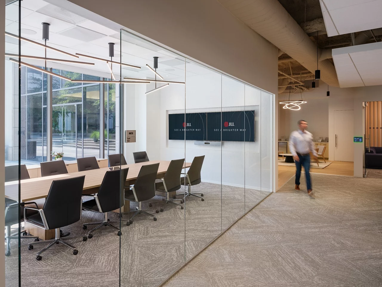 A modern, glass-walled conference room at the JLL Walnut Creek office with JLL branded screens and contemporary lighting.