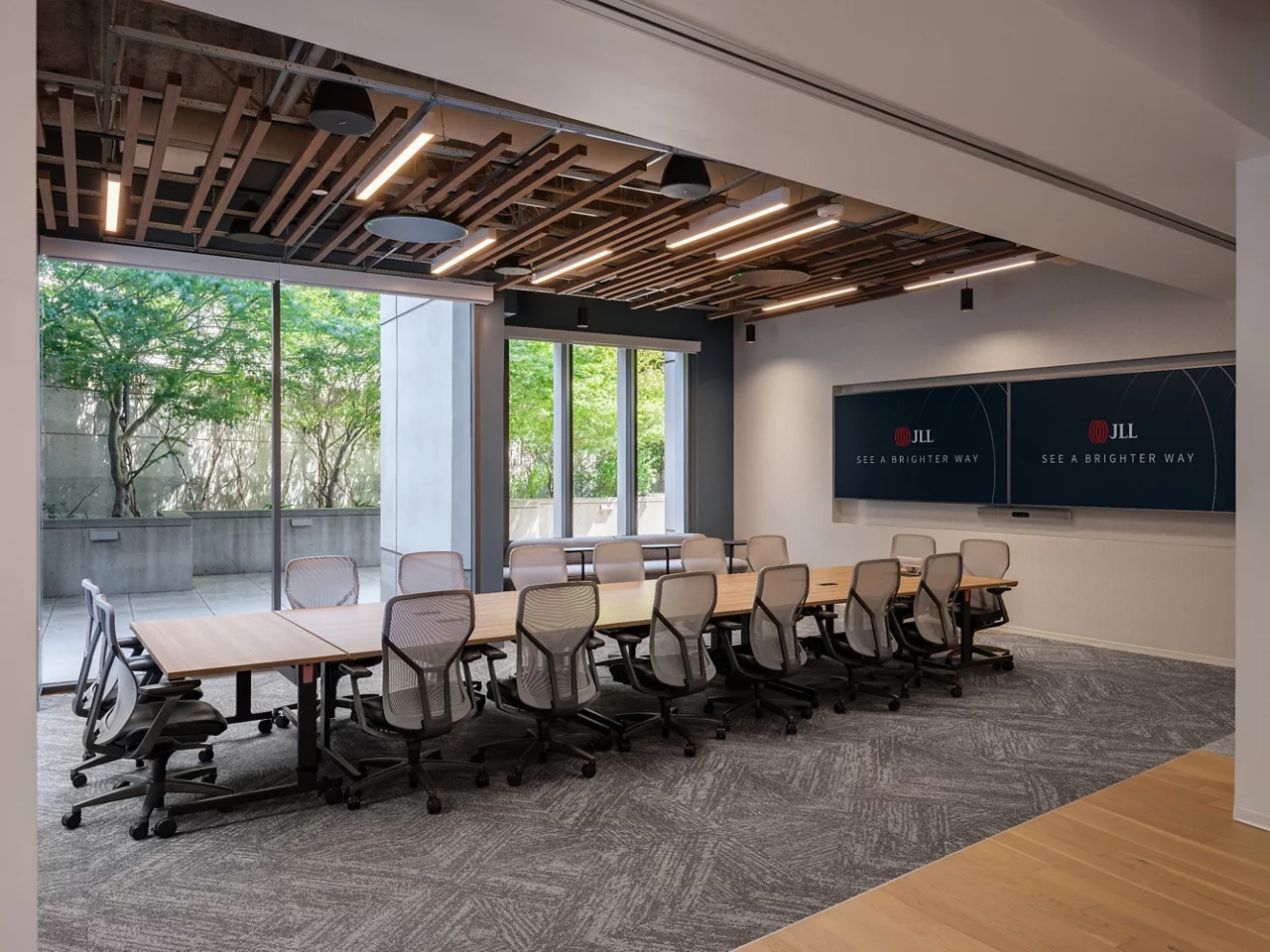 A large conference room in the JLL Walnut Creek office with dual screens, modern seating, and large windows overlooking a patio.