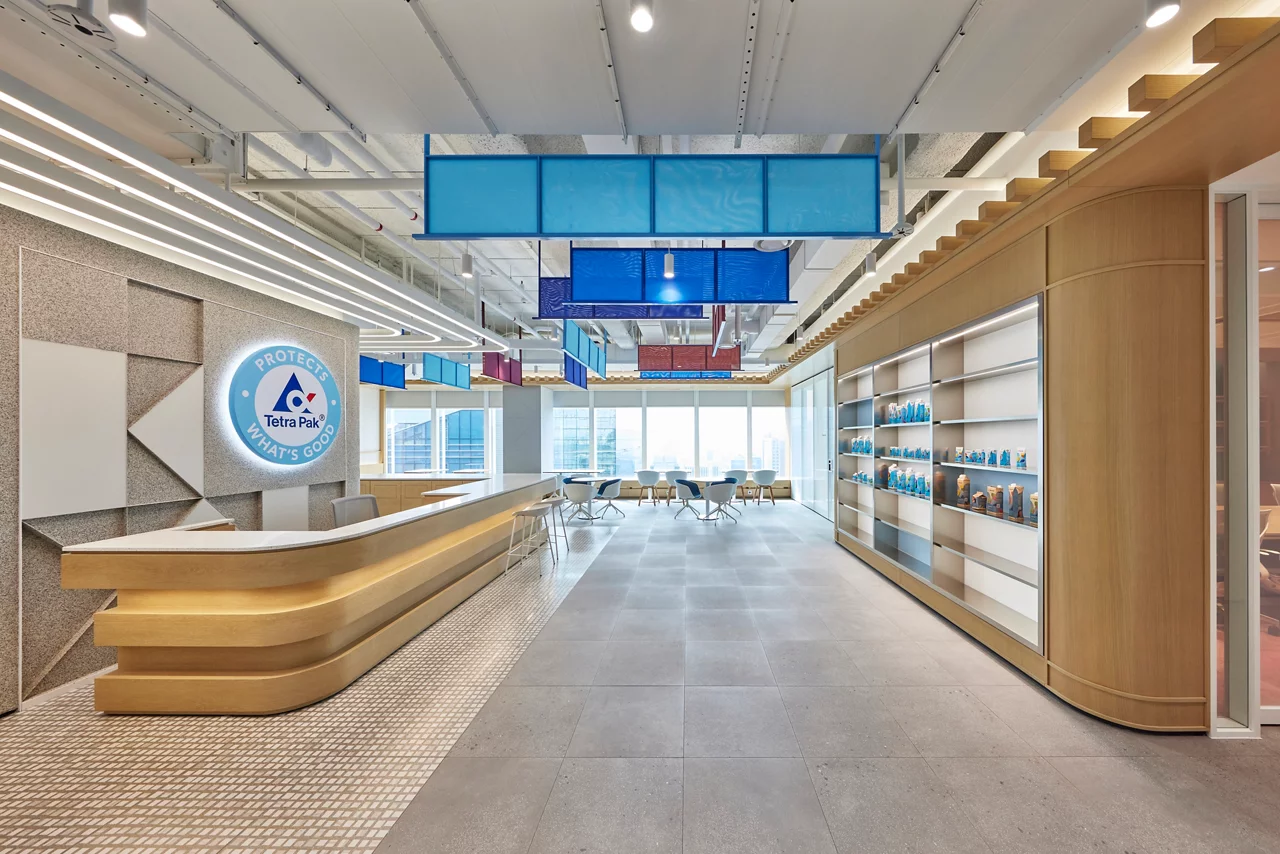The modern Tetra Pak office reception area with a branded logo wall, curved wooden desk, and product display shelving.
