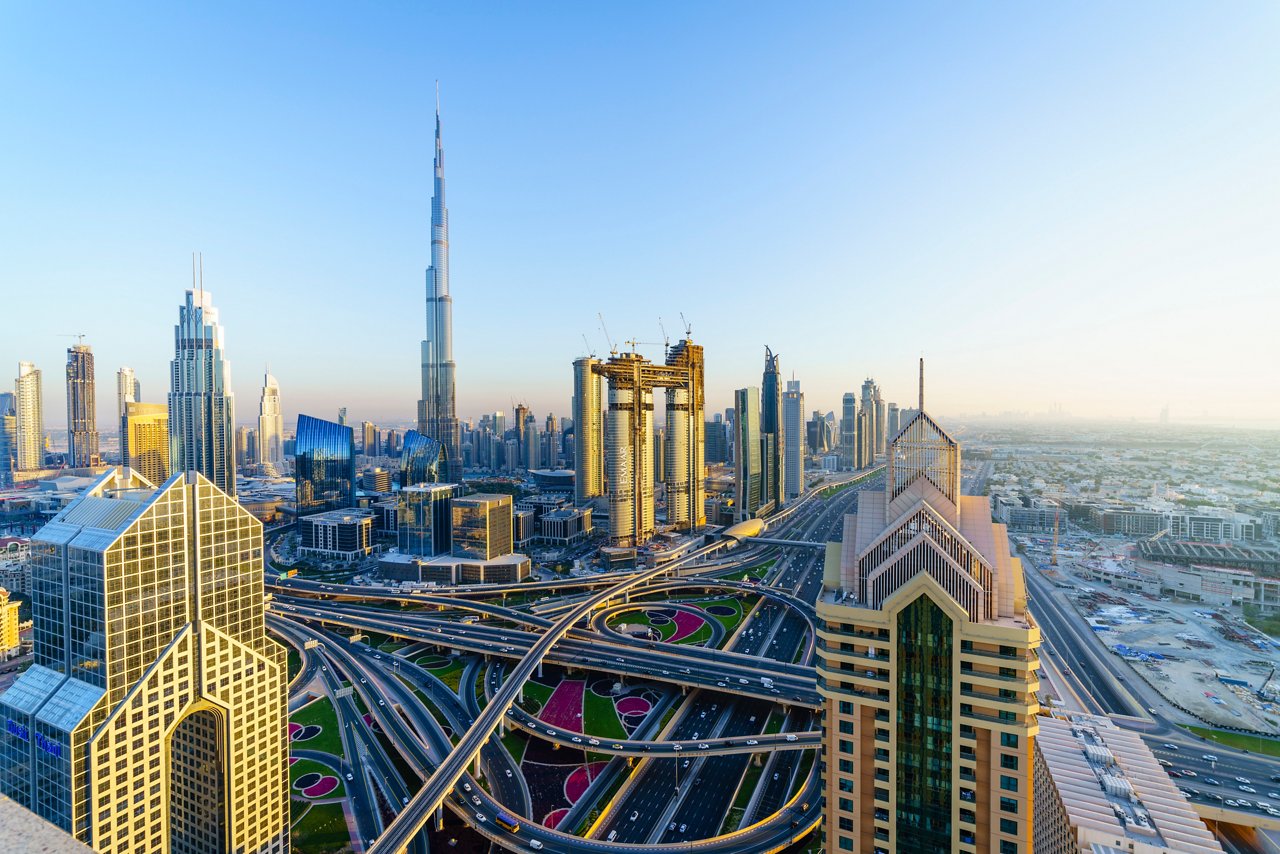 Dubai skyline with Burj Khalifa and modern skyscrapers above busy highways at sunrise.