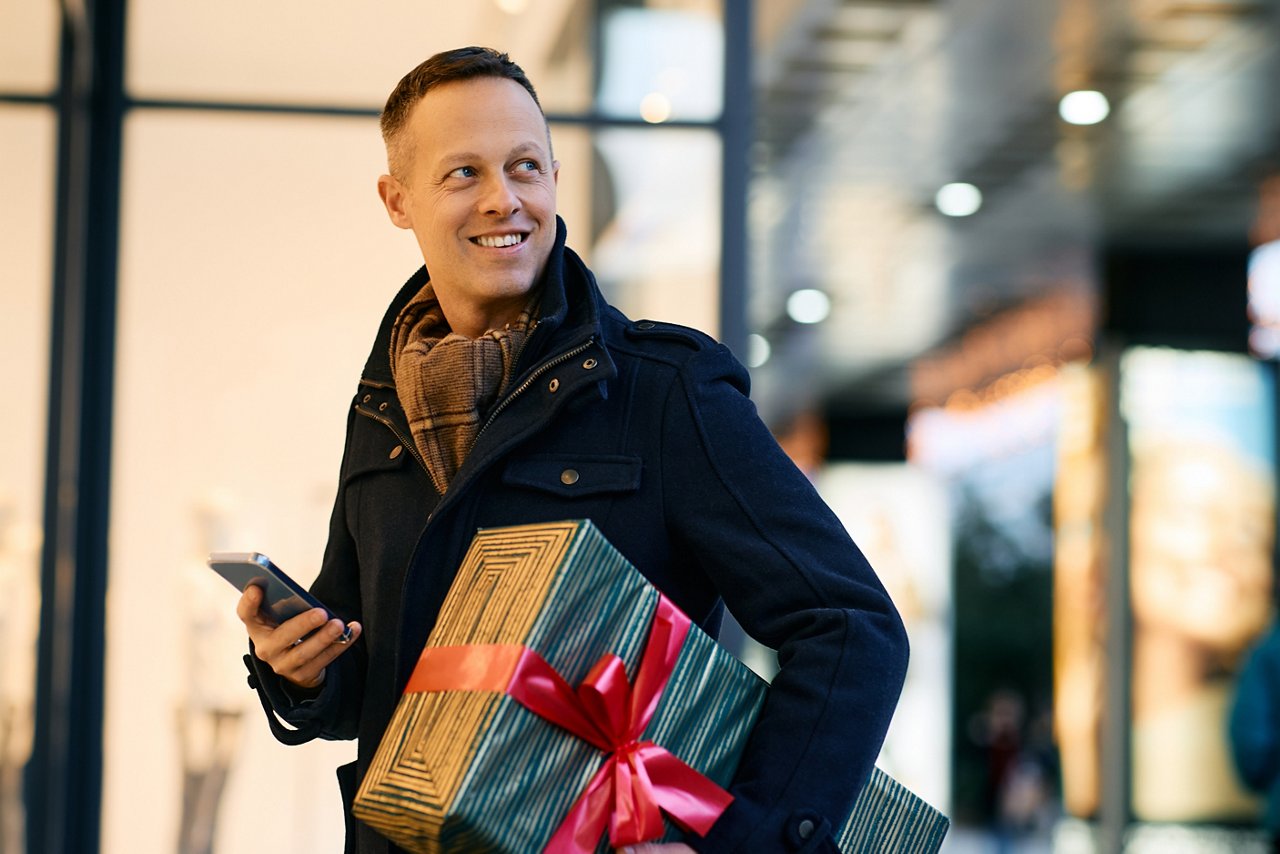 Happy man using smart phone while shopping for Christmas in city.