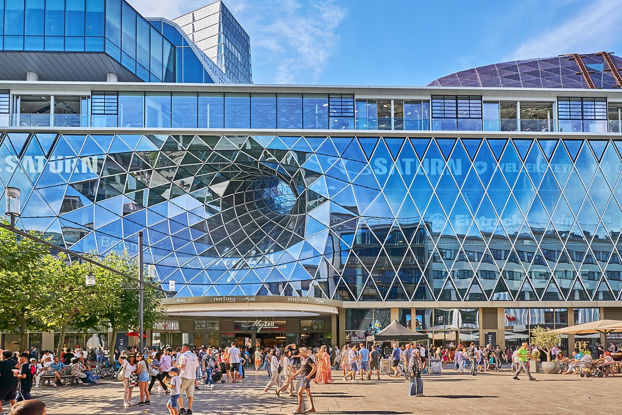In the background a large shopping center with a glass tunnel that runs through the whole building.