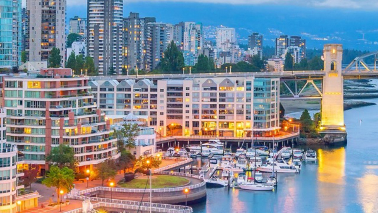 City skyline and marina at dusk with boats and illuminated waterfront buildings.