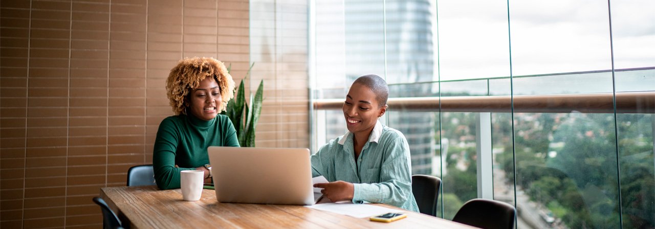 Duas mulheres olhando para o computador com prédios ao fundo